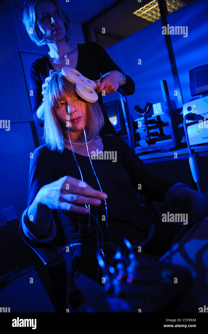 neuroscientist using key shaped paddle to perform transcranial magnetic stimulation TMS on subject sitting in lab Lit blue Stock Photo