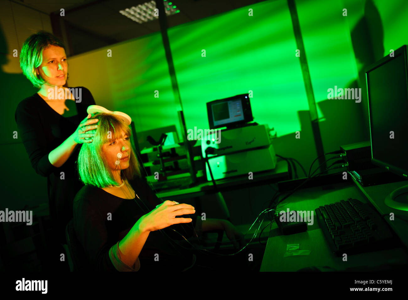neuroscientist using key shaped paddle to perform transcranial magnetic stimulation TMS on subject sitting in lab Lit green Stock Photo