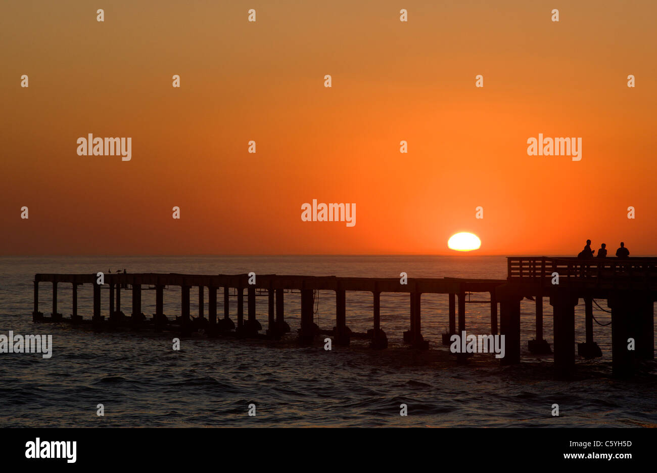Tourists watch the sun setting over the ocean from the pier. Swakopmund, Namibia. Stock Photo