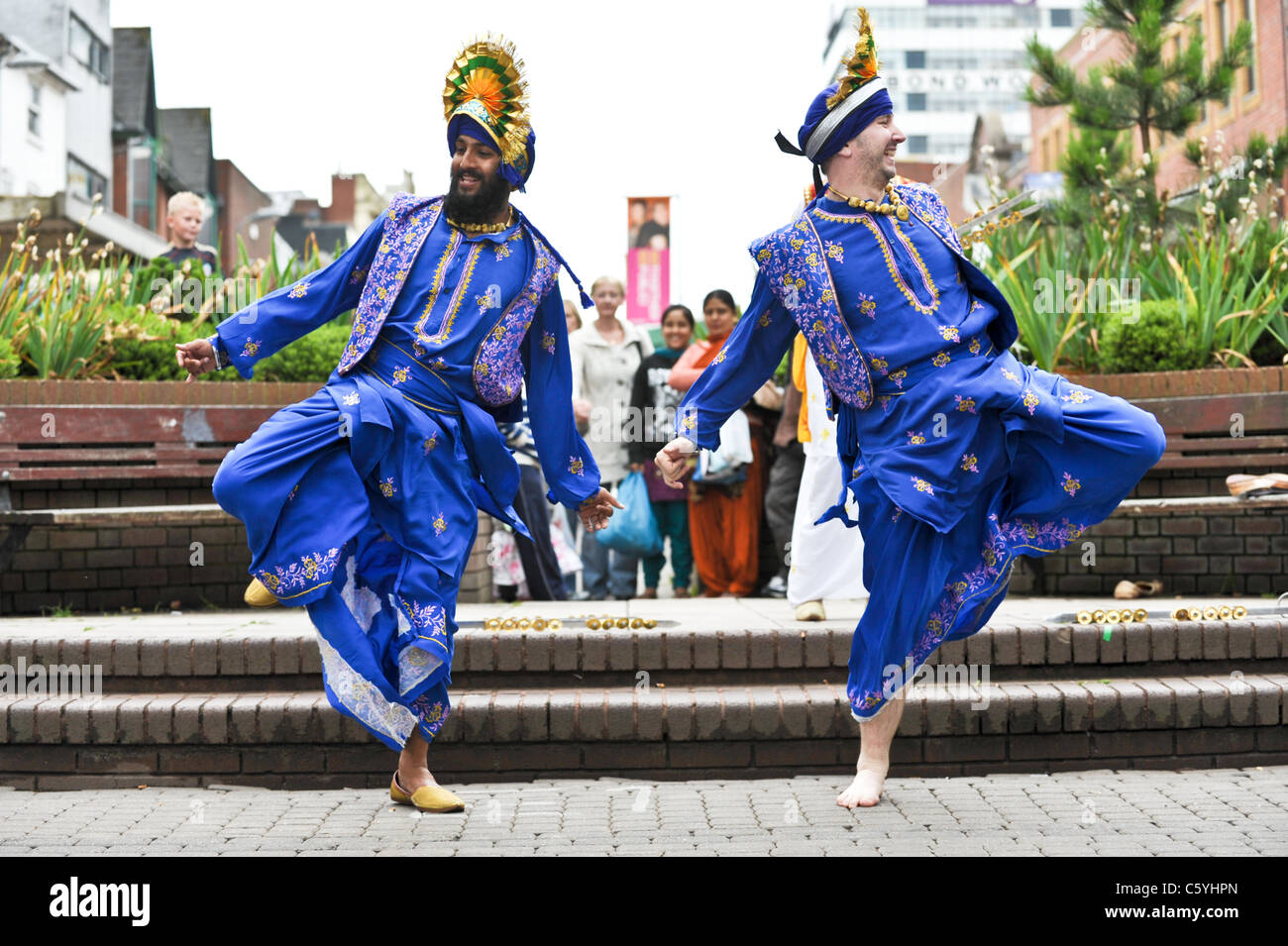 Two Bhangra dancers in traditional colourful and decorative Indian costume in West Bromwich High Street watched by a crowd Stock Photo