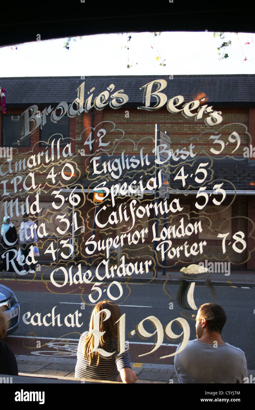Beer prices shown on a window at the William IV pub, with a man and