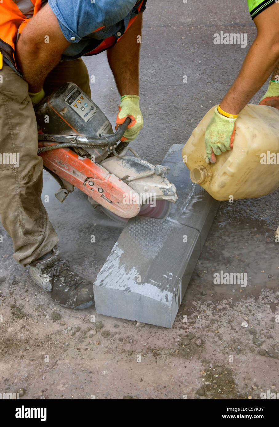 Workmen cutting a kerb-stone with a diamond tipped cutting disc. Stock Photo