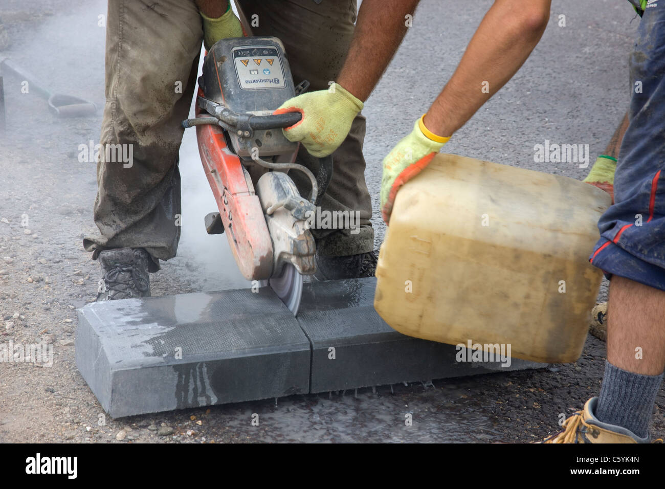 Workmen cutting a kerb-stone  (curb-stone )with a diamond tipped cutting disc. Stock Photo