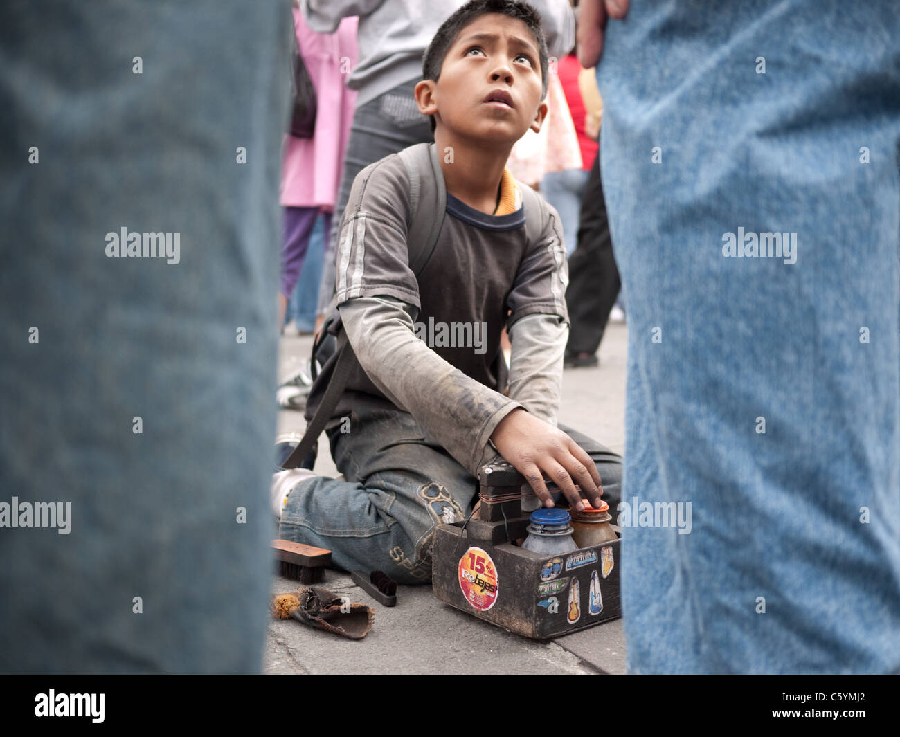 A young shoe shiner looks up at a client while polishing his shoes. Stock Photo