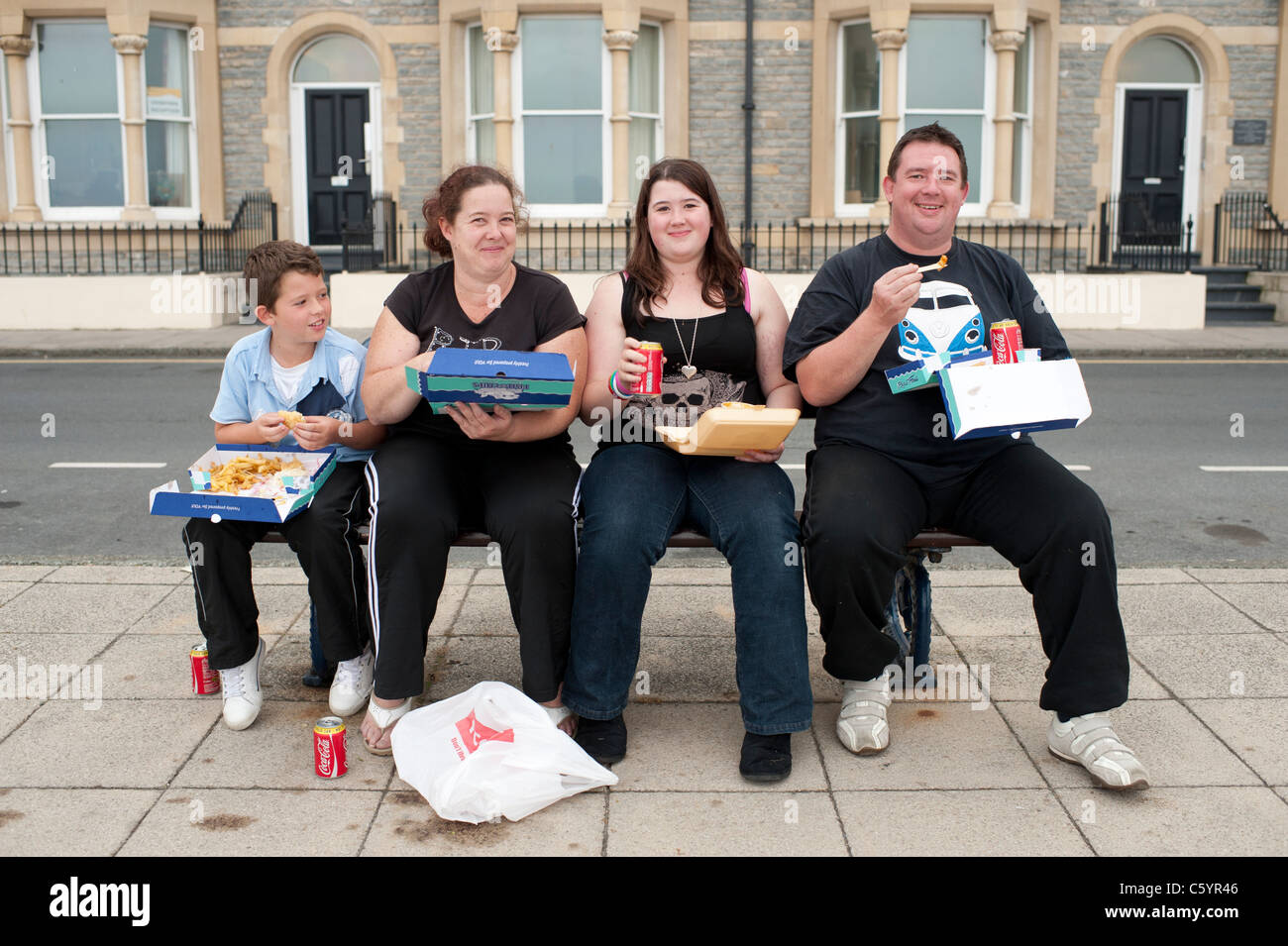 a family - mother, father, daughter, son, eating fish and chips, sitting on a bench, uk Stock Photo