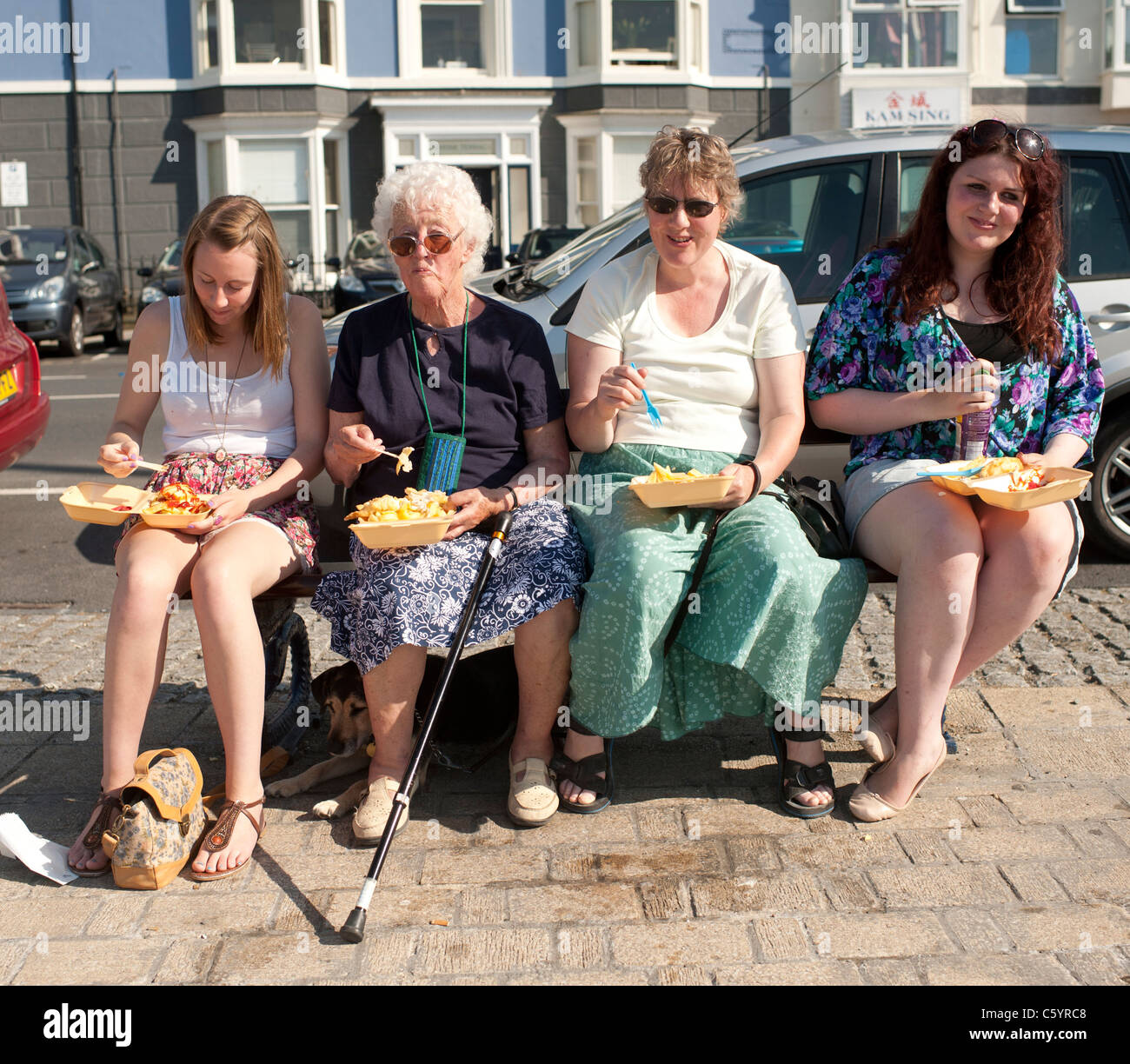 Four women eating fish and chips sitting on a bench at Aberystwyth Ceredigion Wales UK Stock Photo