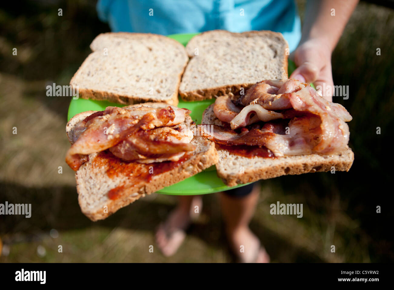 Person holding bacon sandwiches with BBQ sauce, camping, Cornwall, England Stock Photo Alamy