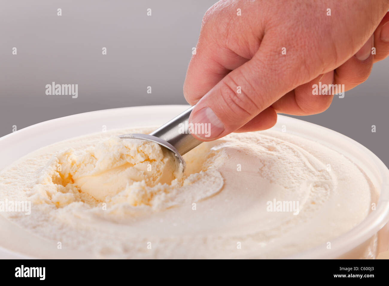 Mans hand scooping vanilla ice cream from tub Stock Photo Alamy
