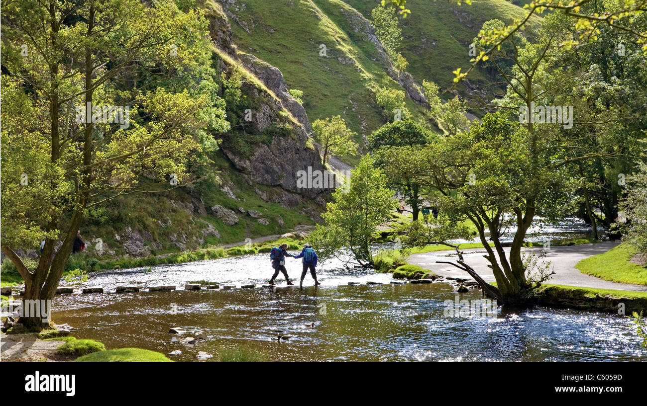 A couple of walkers struggle to cross the stepping stones over the River Dove at Thorpe Cloud in Dovedale Derbyshire Stock Photo