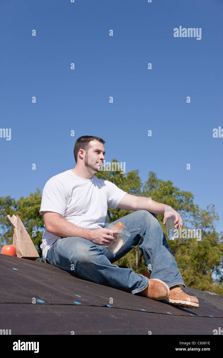 USA, Illinois, Metamora, Young man sitting on roof and eating lunch ...
