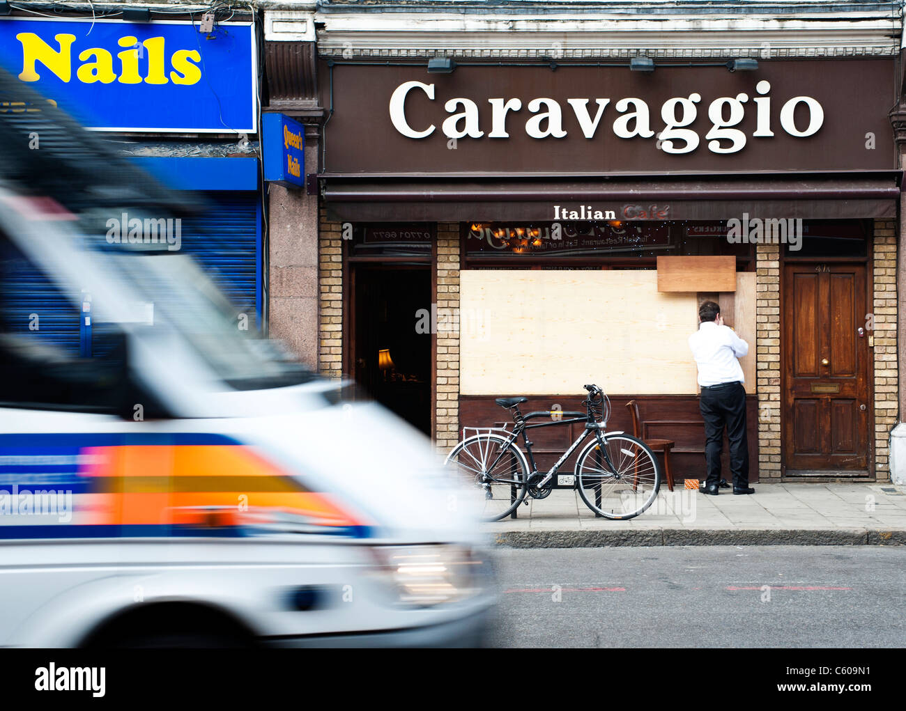 Restaurant owner boarding up his property during the London Riots as a police van rushes by. Stock Photo