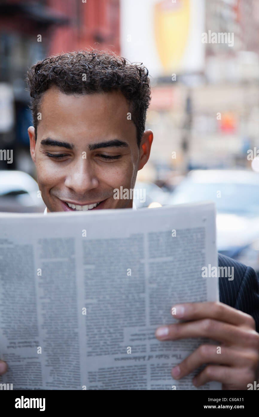 USA, New York, New York City, smiling businessman reading newspaper on street Stock Photo