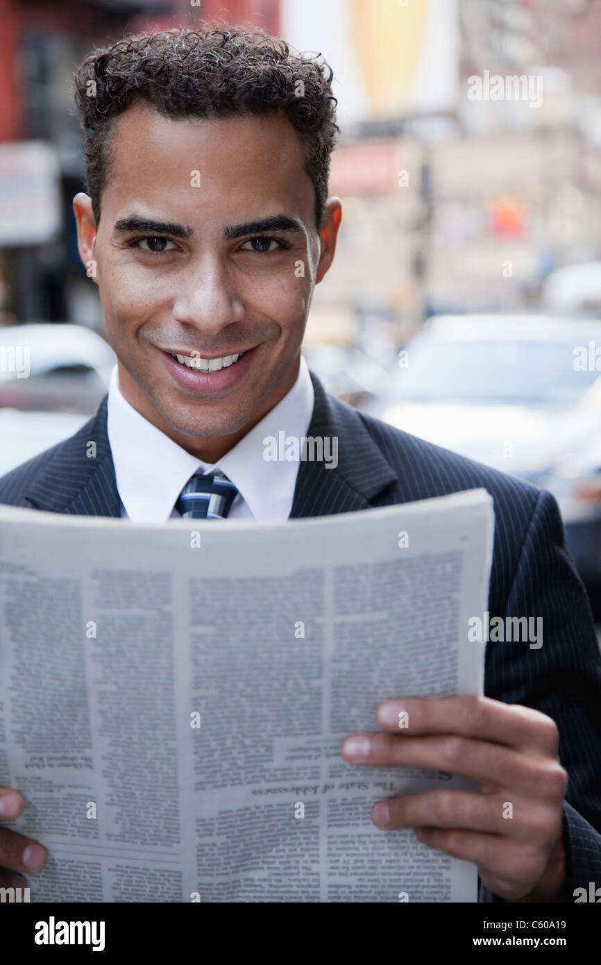 USA, New York, New York City, portrait of smiling businessman holding newspaper on street Stock Photo