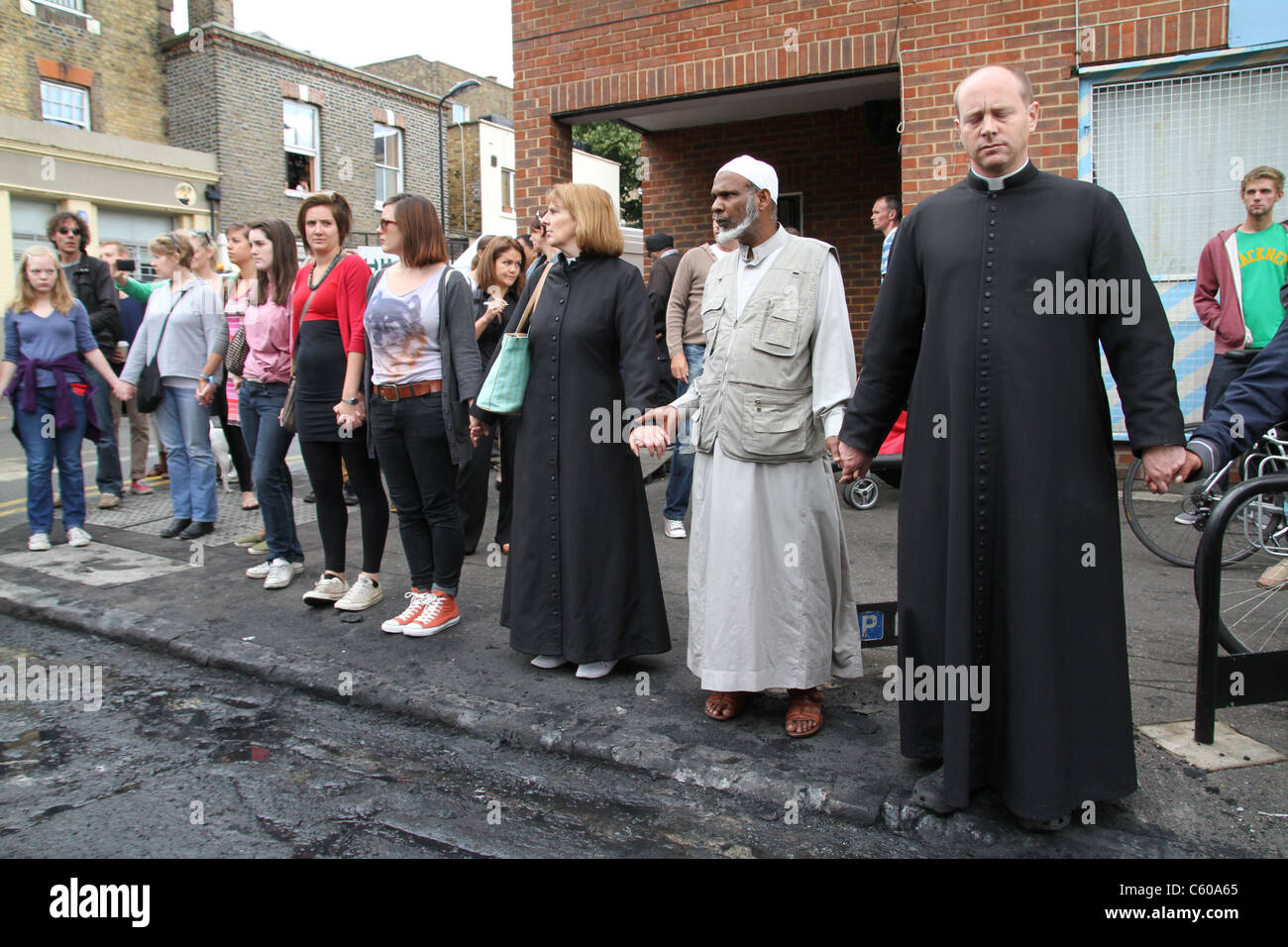 Local community get together to clear damage caused by rioters and looters in Hackney, London.Christian and Muslim leaders pray. Stock Photo