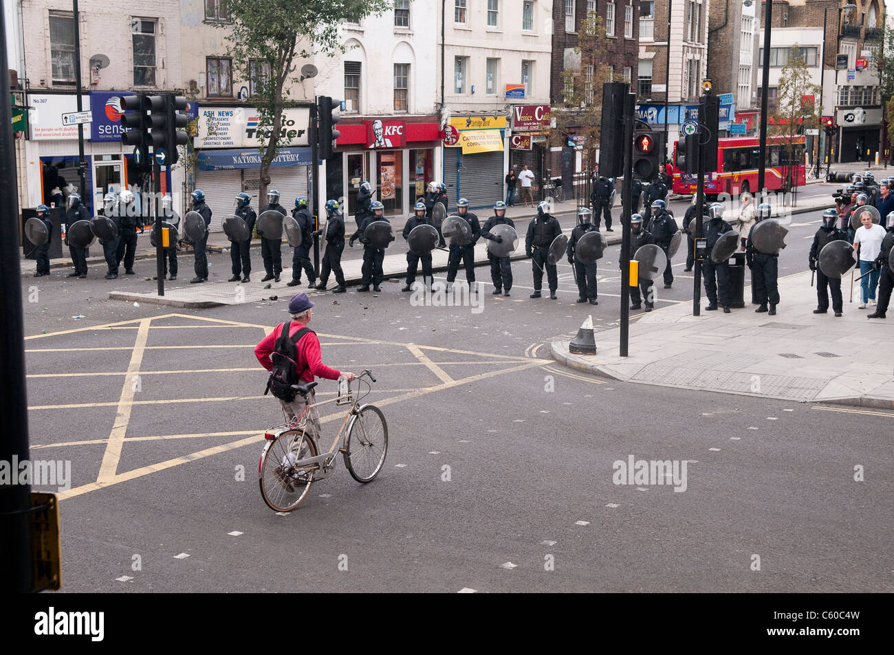 Man with a bicycle waking towards a line of riot police on Mare Street during London Riots - Hackney Central, 8/8/2011 Stock Photo