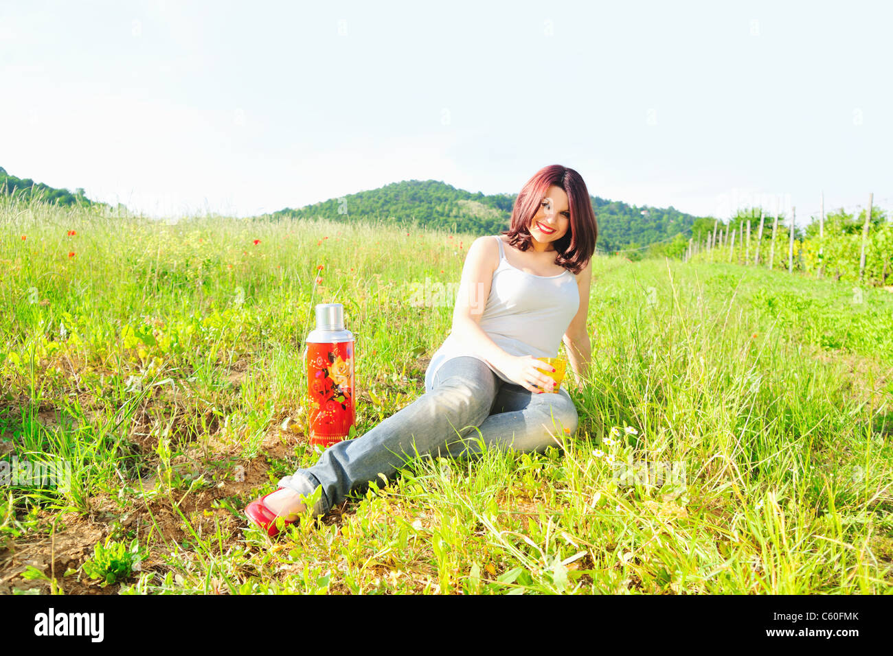 Woman drinking from thermos in field Stock Photo