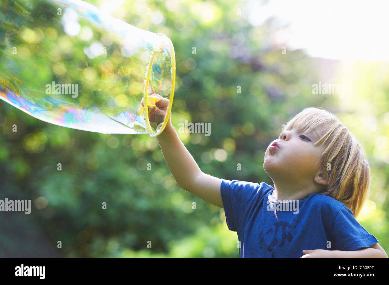 Boy blowing oversized bubble in backyard Stock Photo