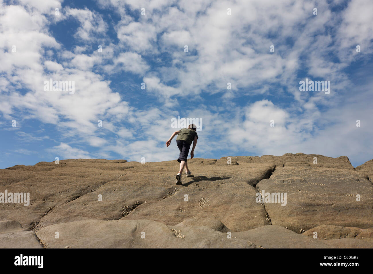 A 13 year-old teenage boy walks up steep sandstone rocks in the coastal cove of Trentishoe in north Devon. Stock Photo