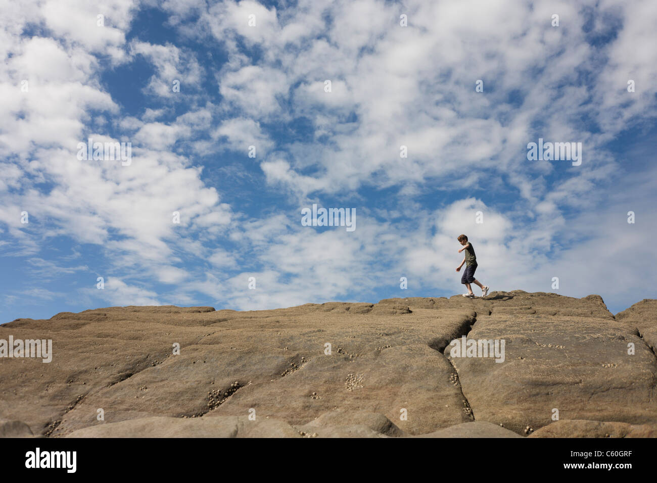 A 13 year-old teenage boy walks along the tops of sandstone rocks in the coastal cove of Trentishoe in north Devon. Stock Photo