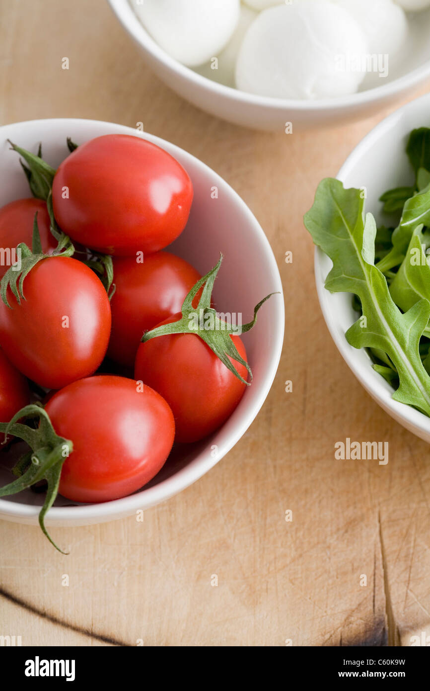Tomatoes, greens and mozzarella in bowls Stock Photo