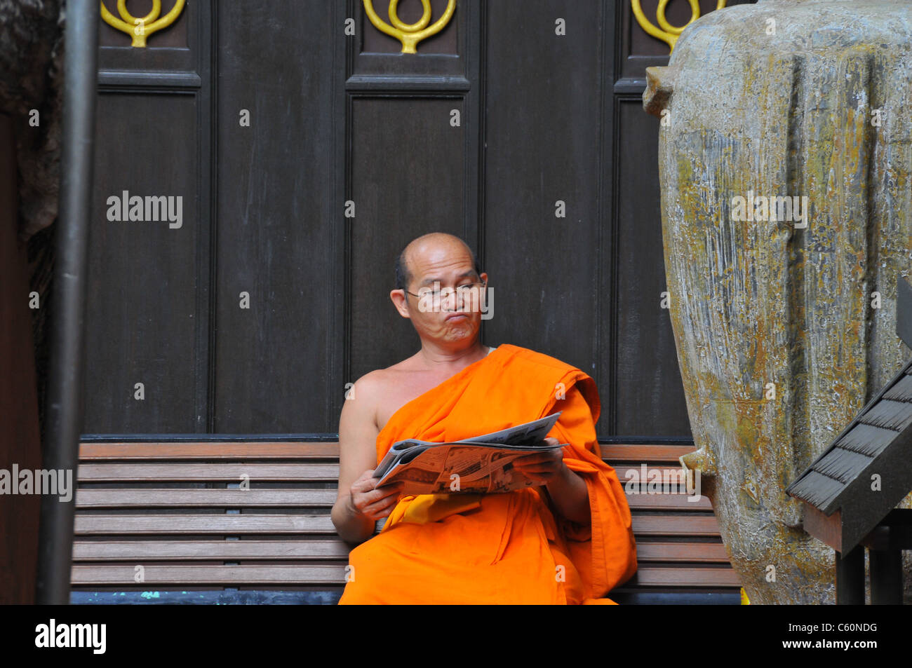 one man bonze buddhist outside of a temple reading a newspaper with glasses and doubtful Stock Photo