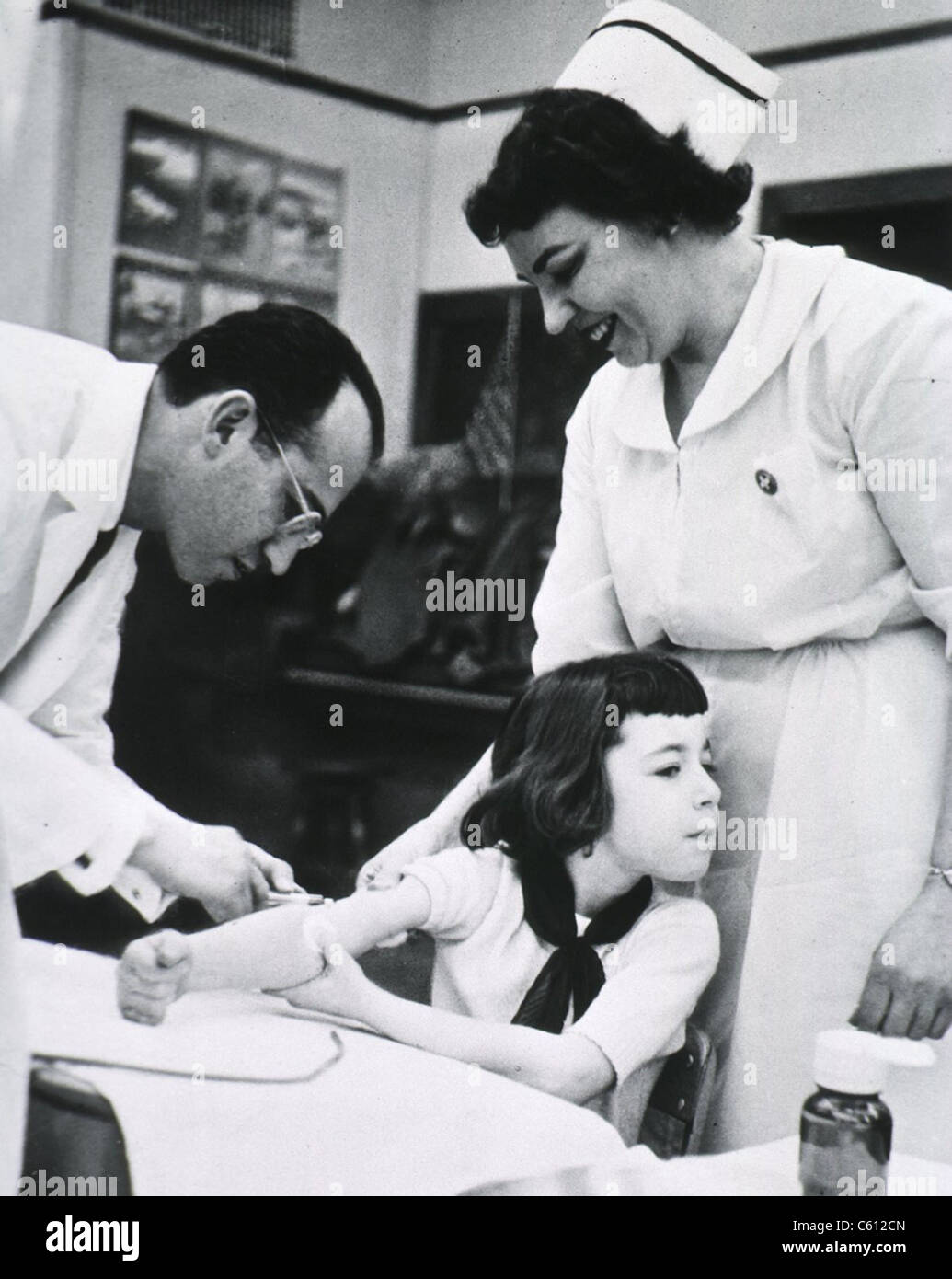 Jonas E. Salk (1914-1995), American physician who developed the first effective Polio vaccine inoculating child as nurse stands Stock Photo