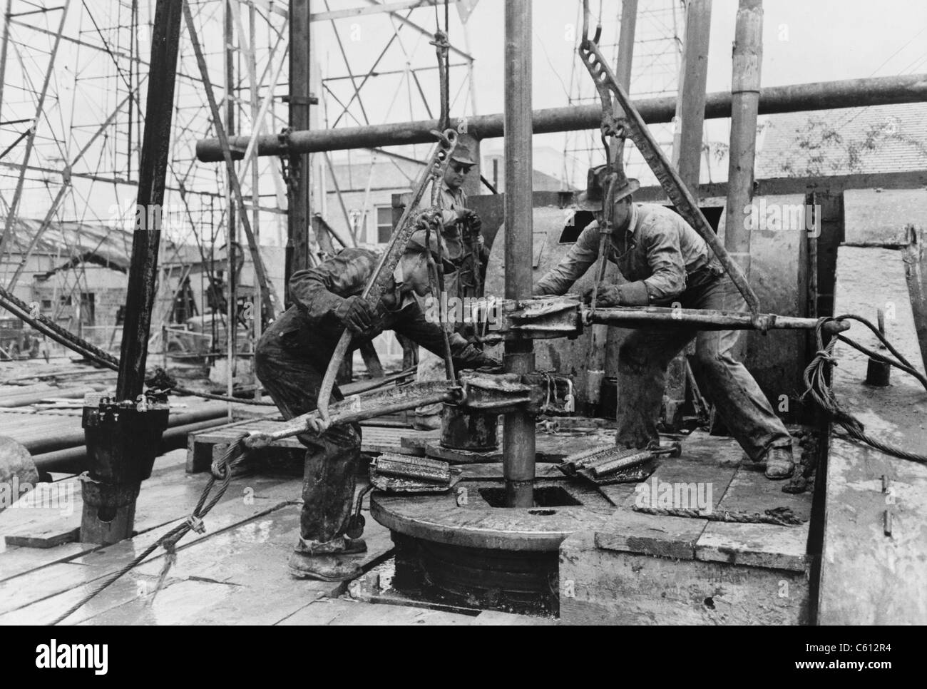 Oil rig workers, called roughnecks, at work, loosening sections of pipe