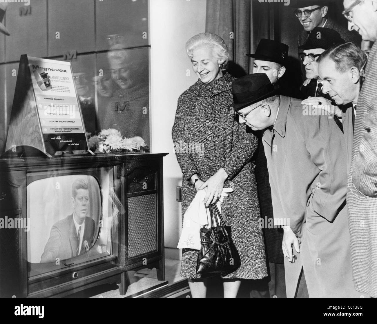 People gather around a television outside a store window on a New York street as President John F. Kennedy speaks during a press conference on November 21, 1962. The new Magnavox TV used transistors instead of vacuum tubes and featured a remote control. Stock Photo