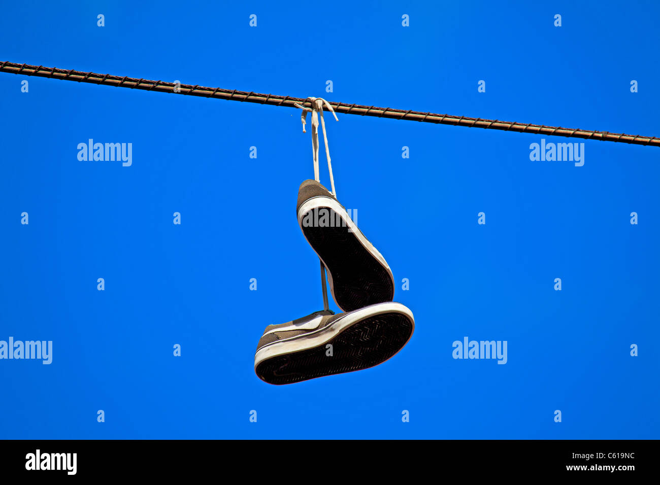 tennis shoes hanging from a power line against clear blue sky. Stock Photo