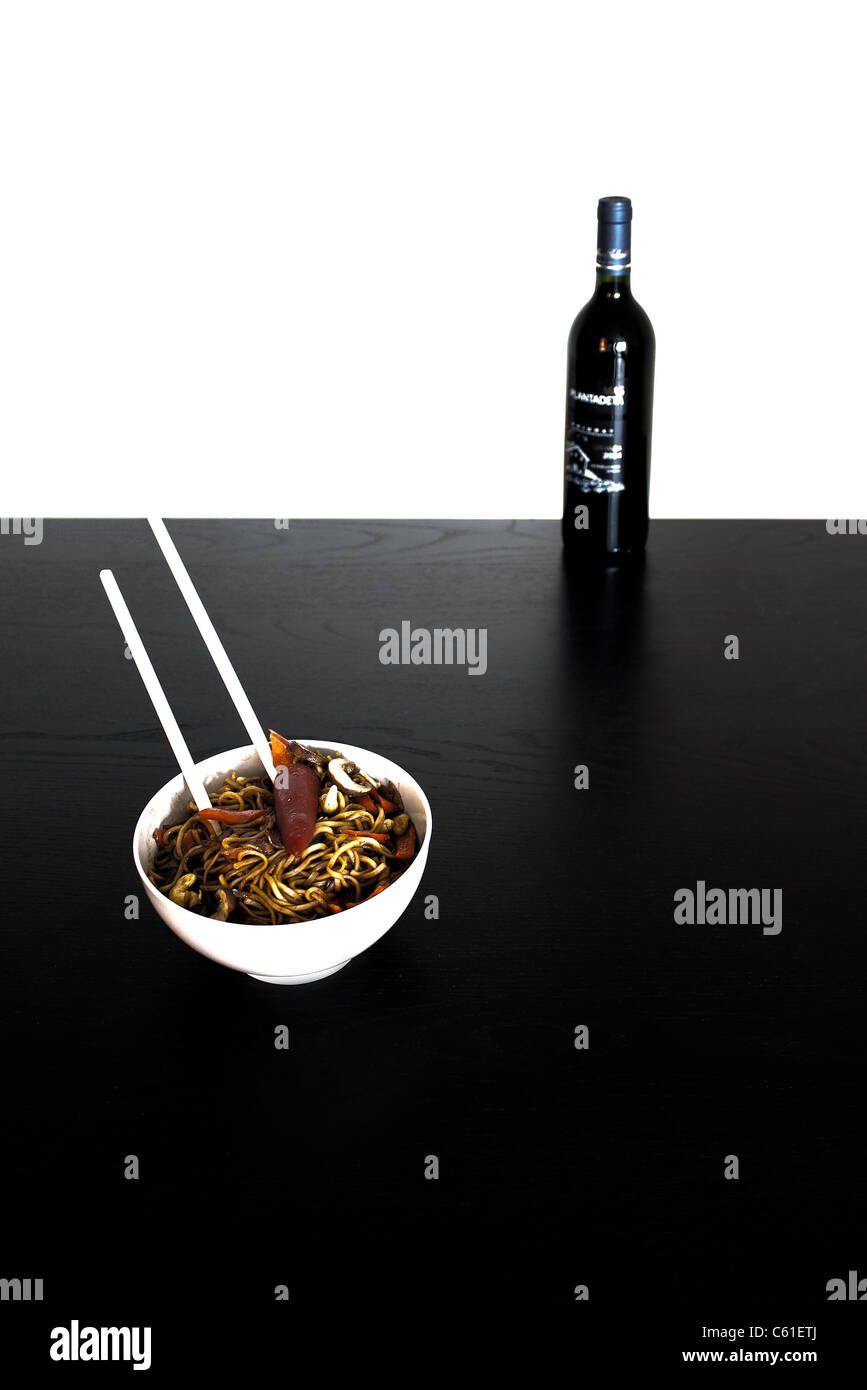 Bowl of noodles with chopsticks in front of a bottle of wine. Slightly abstract picture with