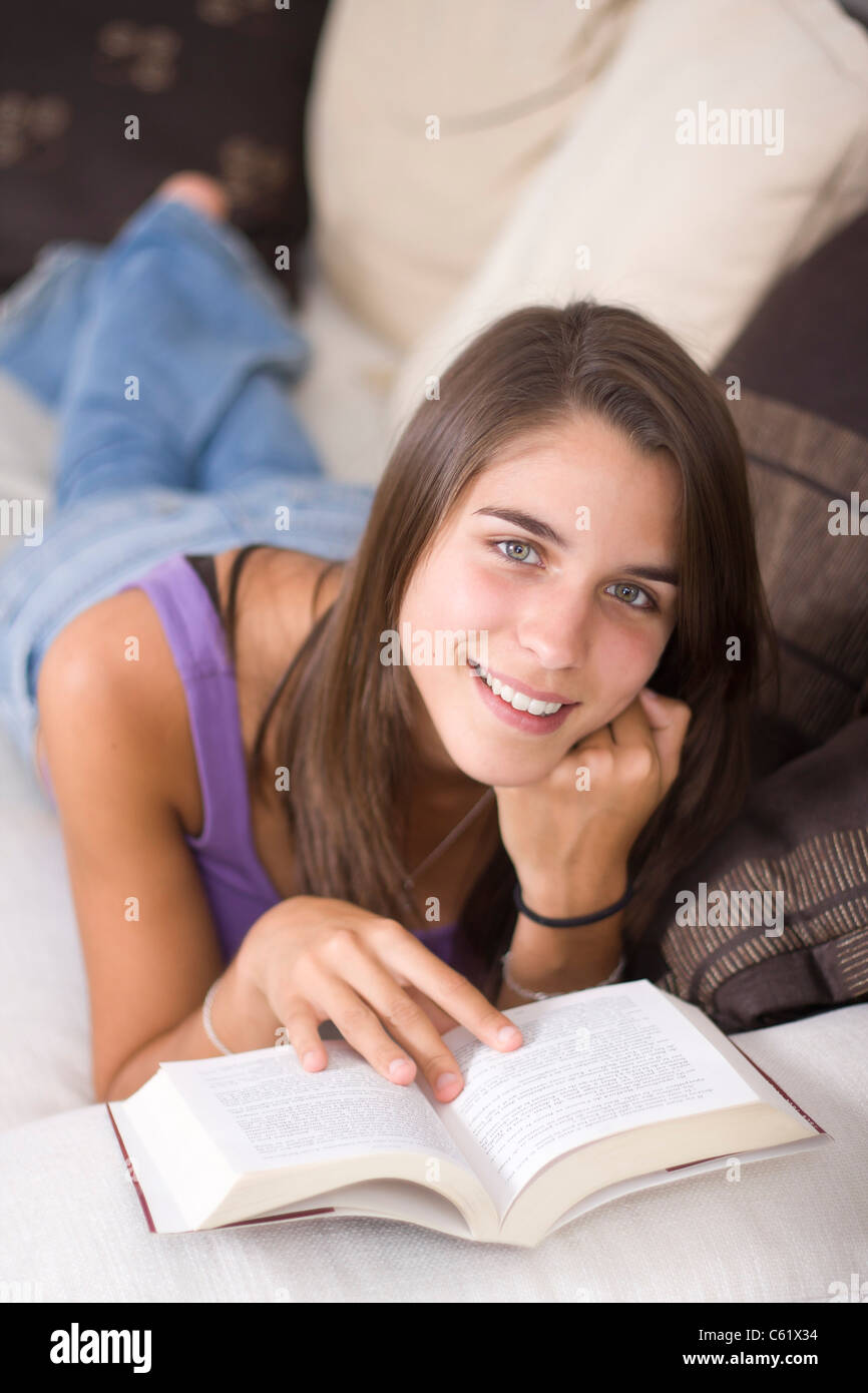 A cute young woman lying on a couch reading a book Stock Photo - Alamy