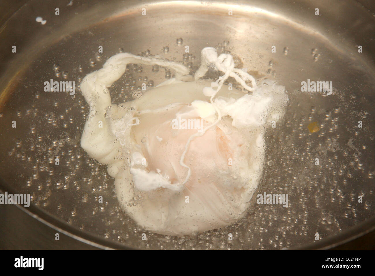 An egg being poached in boiling water. Stock Photo