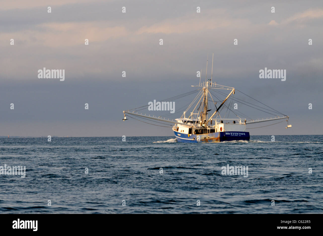 Blue hulled fishing boat fishing off the coast of Cape Cod with outriggers extended headed out to sea on a stormy day. USA Stock Photo