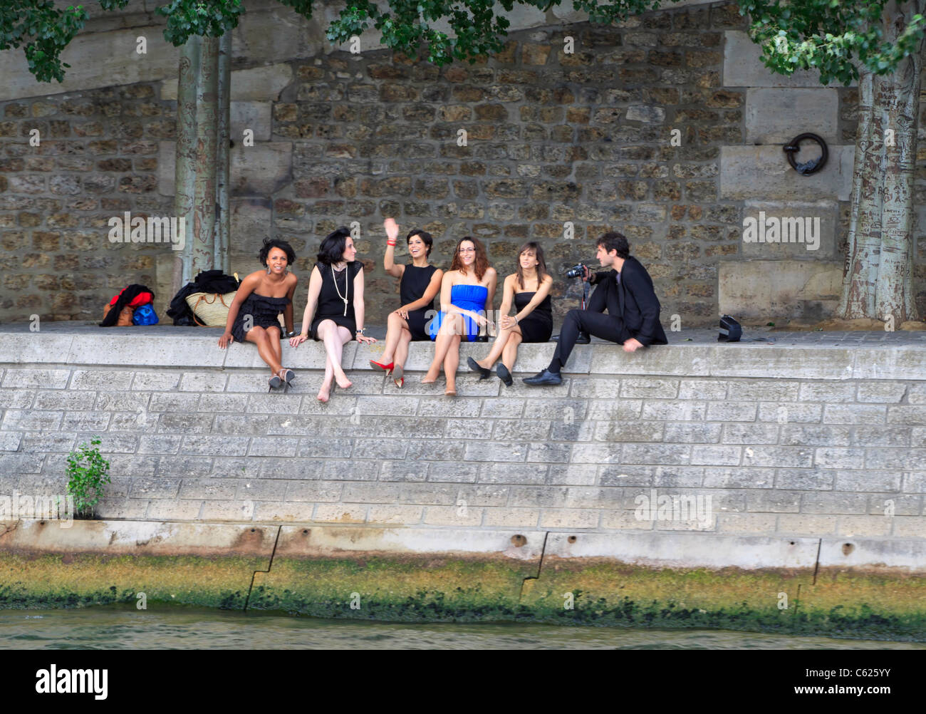 Five women and a photographer sit on the bank of the Seine River, Paris Stock Photo