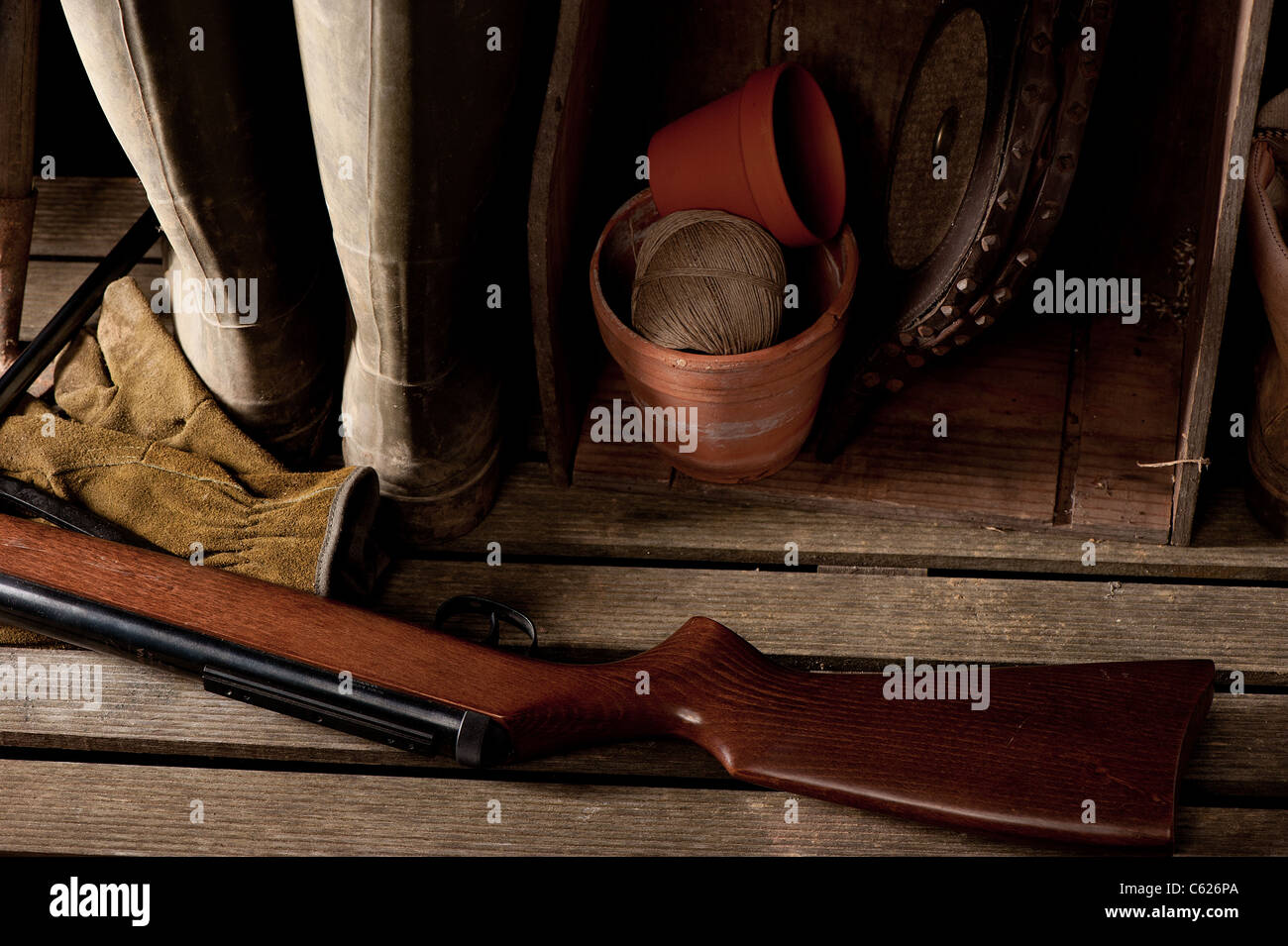 Boots and rifle in dimly lit garden shed Stock Photo