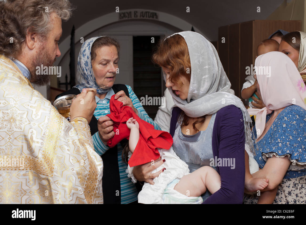 Baby baptism in Russian orthodox church. Priest christening the little child. Godmother holding infant in hands. Russia Stock Photo