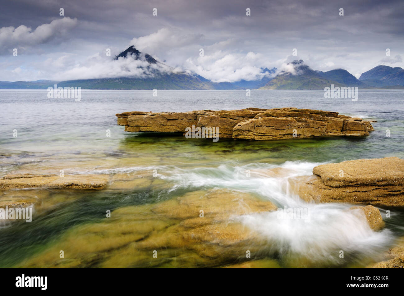 Swirling waves at Elgol on the Isle of Skye with cloud cloaked Black Cuillin mountains in the background Stock Photo