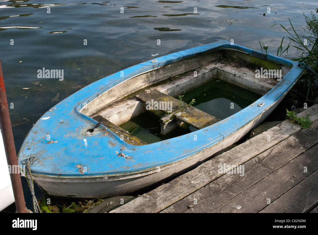Flooded halfsunken old rowing boat tied to a dock on a river Stock