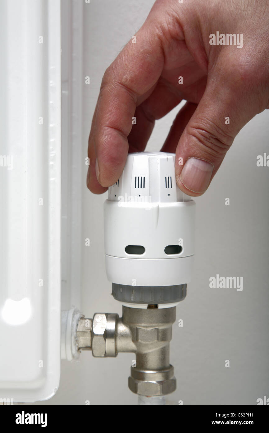 Hand adjusting a thermostatic central heating radiator valve. Stock Photo