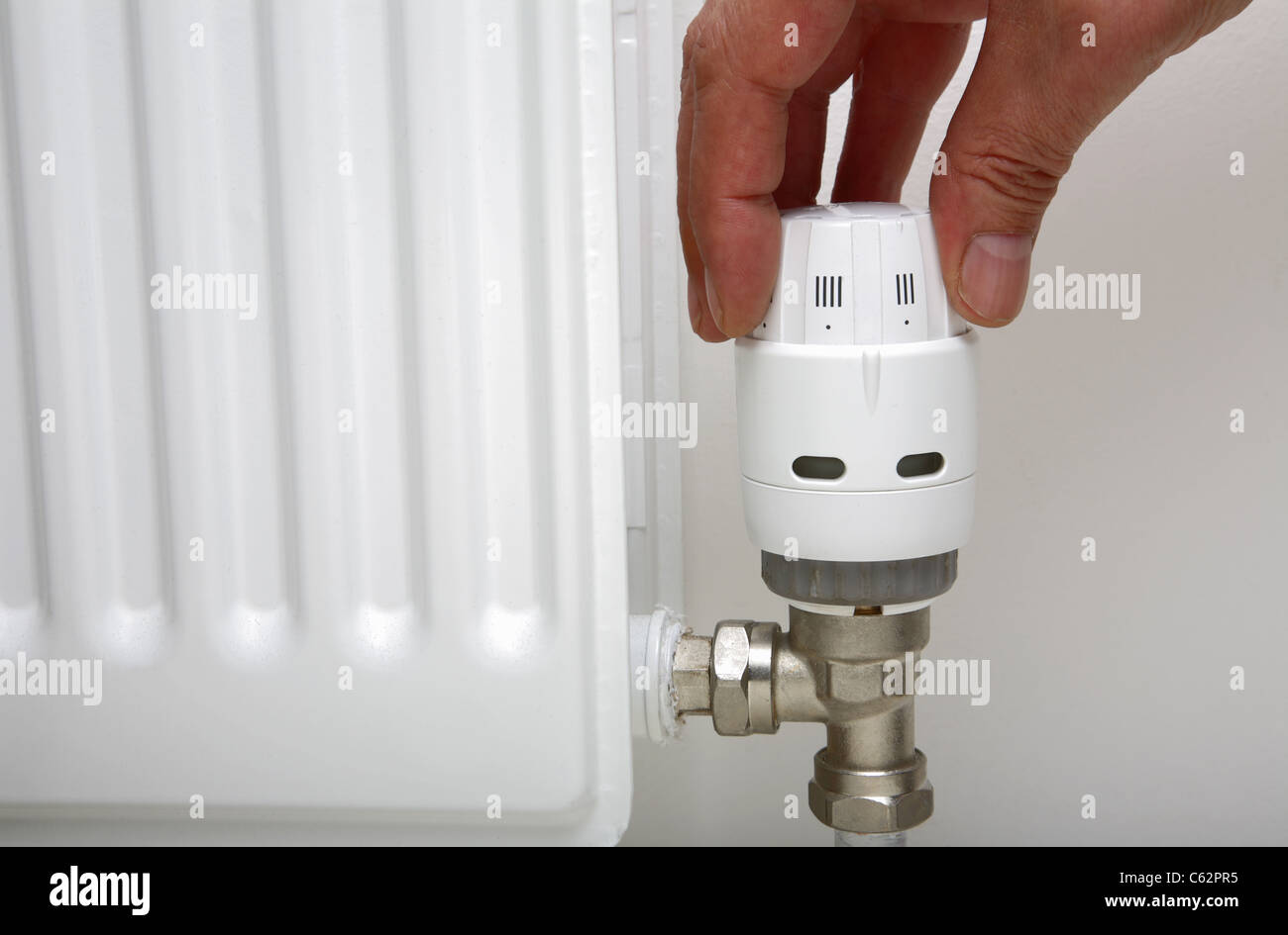Hand adjusting a thermostatic central heating radiator valve. Stock Photo