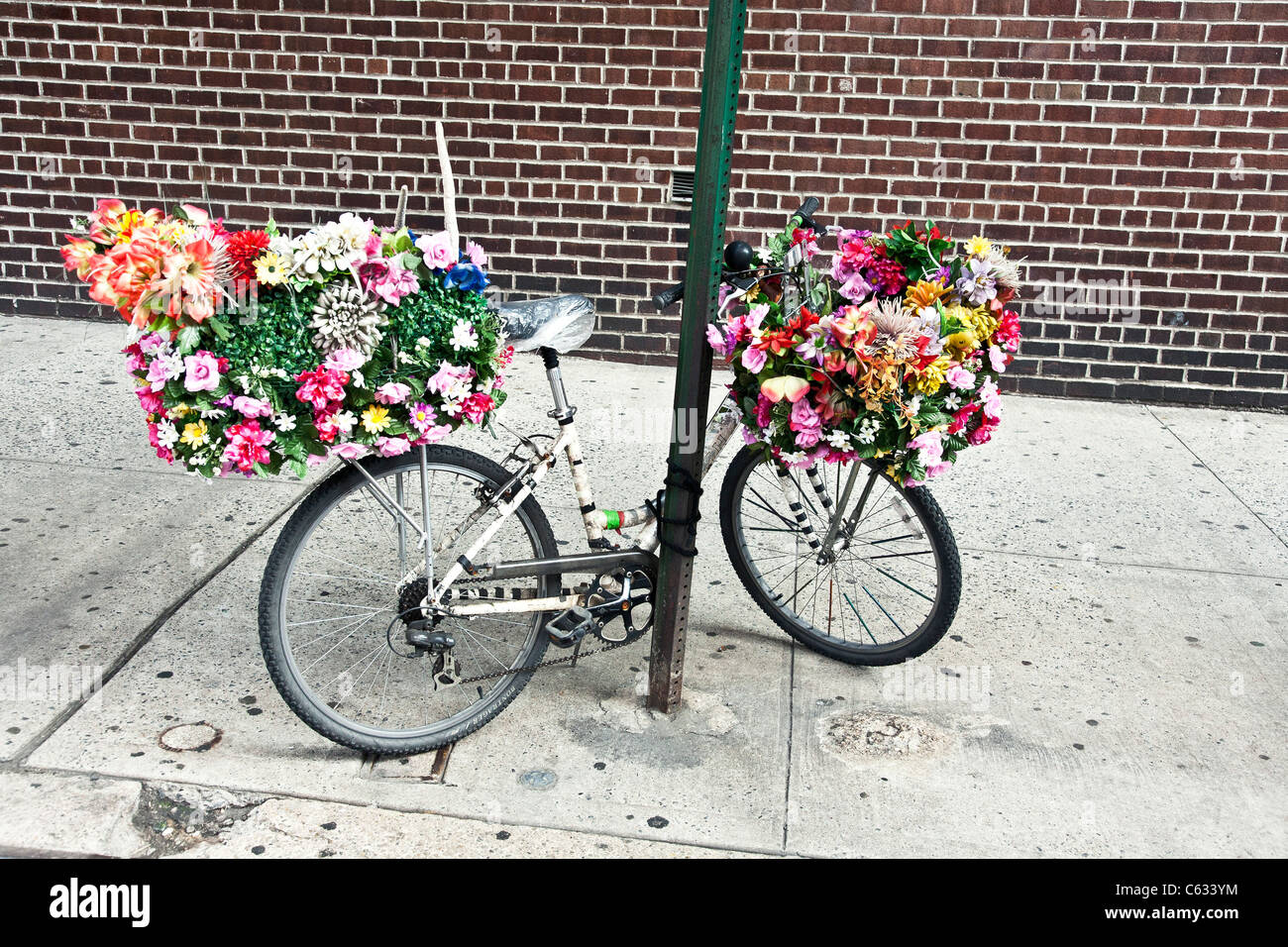 delivery bicycle with baskets heavily decorated with bright plastic flowers parked  west side Manhattan sidewalk New York City Stock Photo