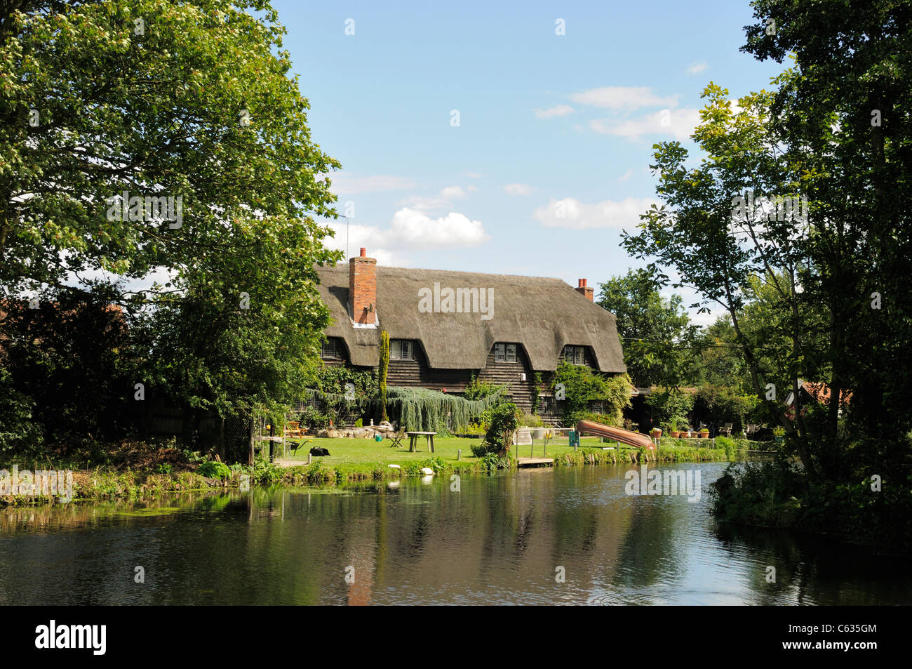 A large thatched cottage next to a river bank at Flatford on the border of Suffolk and Essex, England. Stock Photo