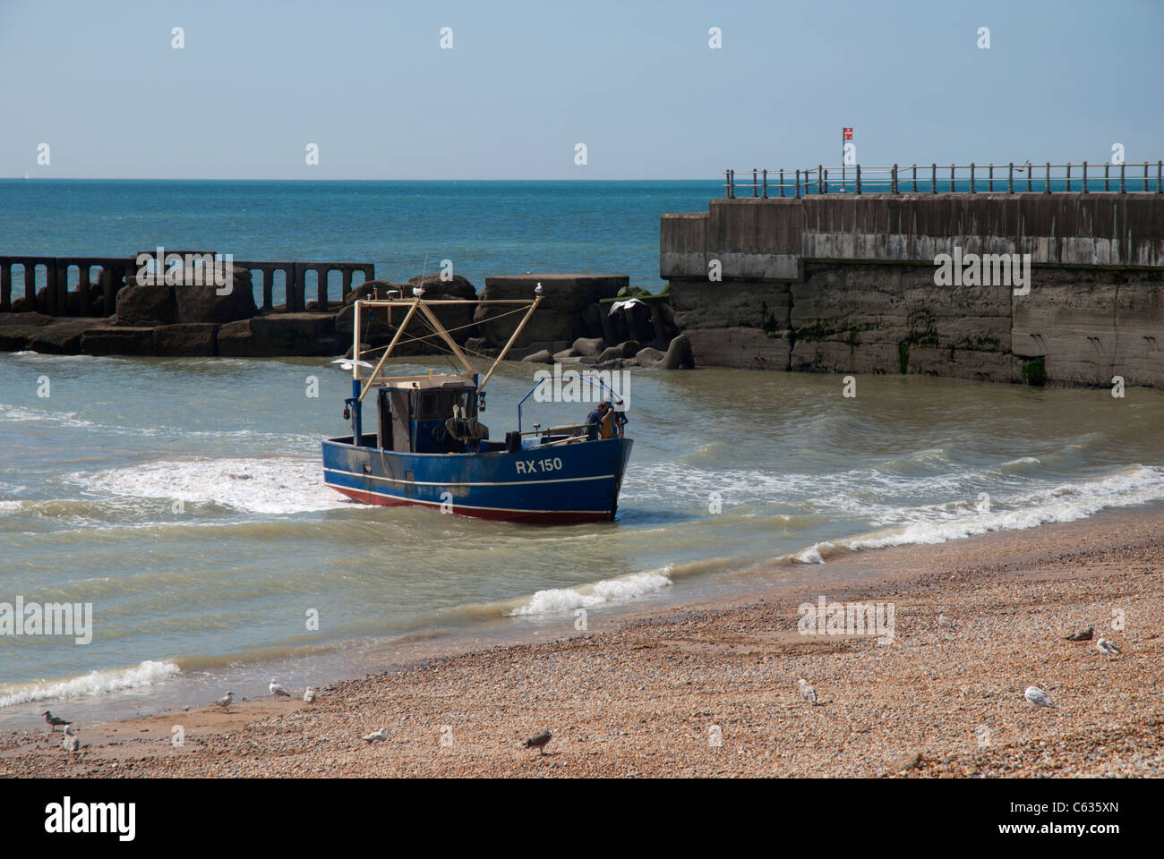 Hastings has the largest beach-based fishing fleet in England. A returning fishing boat waiting to be winched up onto the beach. Stock Photo
