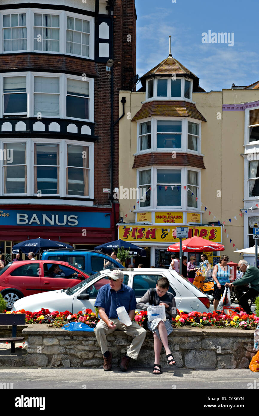 Two people eating near to a fish and chip shop at a seaside resort in England Stock Photo
