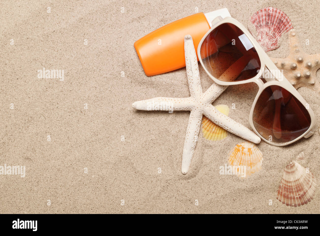 Bottle of balm solar with shells and sunglasses on sand Stock Photo