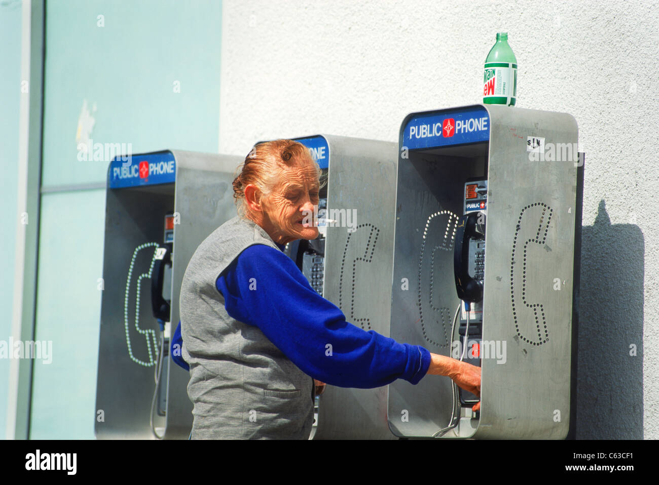 Elderly destitute woman smoking cigarette and looking for money at public phones  in downtown Los Angeles Stock Photo