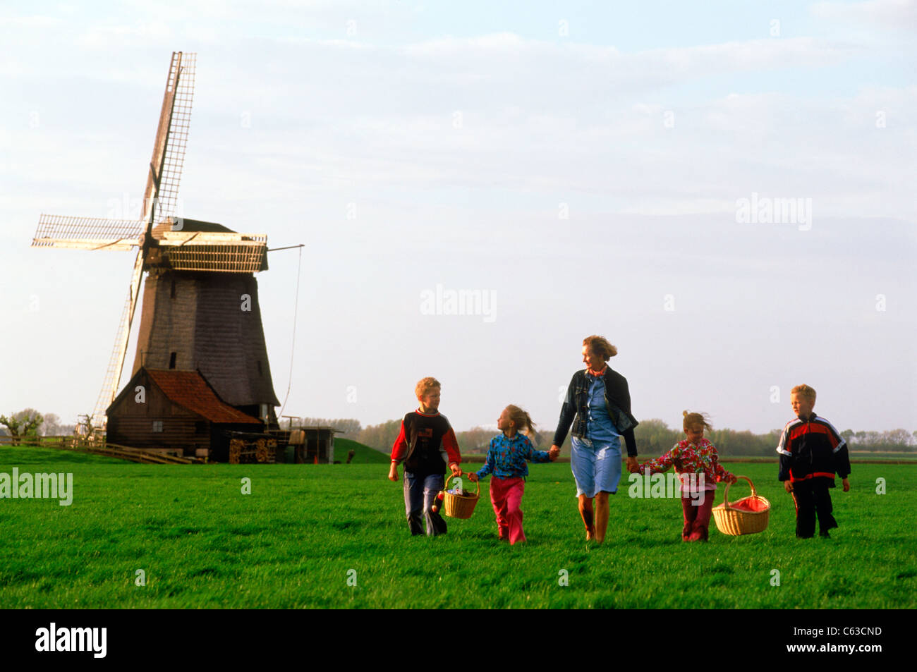 Mother and children with baskets crossing farmlands in Holland near windmill Stock Photo