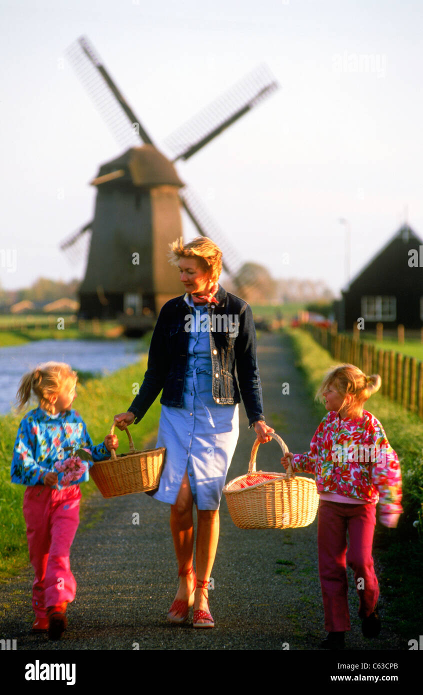 Mother with two daughters and baskets walking home in Holland along canal with windmill Stock Photo