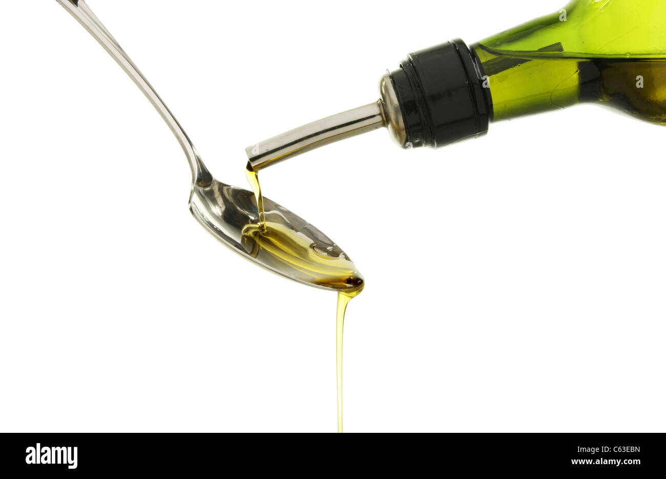 Olive oil pouring onto a spoon from a green bottle against a white background Stock Photo