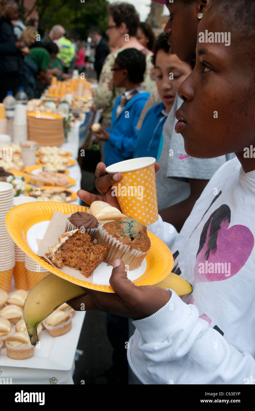 Clarence Road Hackney. Street tea party one week after the riots.Young black girl and others help themselves to cakes Stock Photo